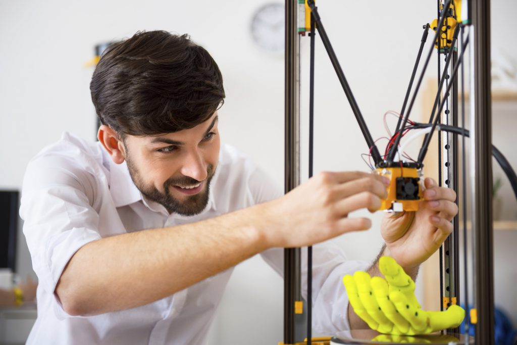 Crafty hands. Cheerful delighted smiling man using 3d printer and expressing positivity